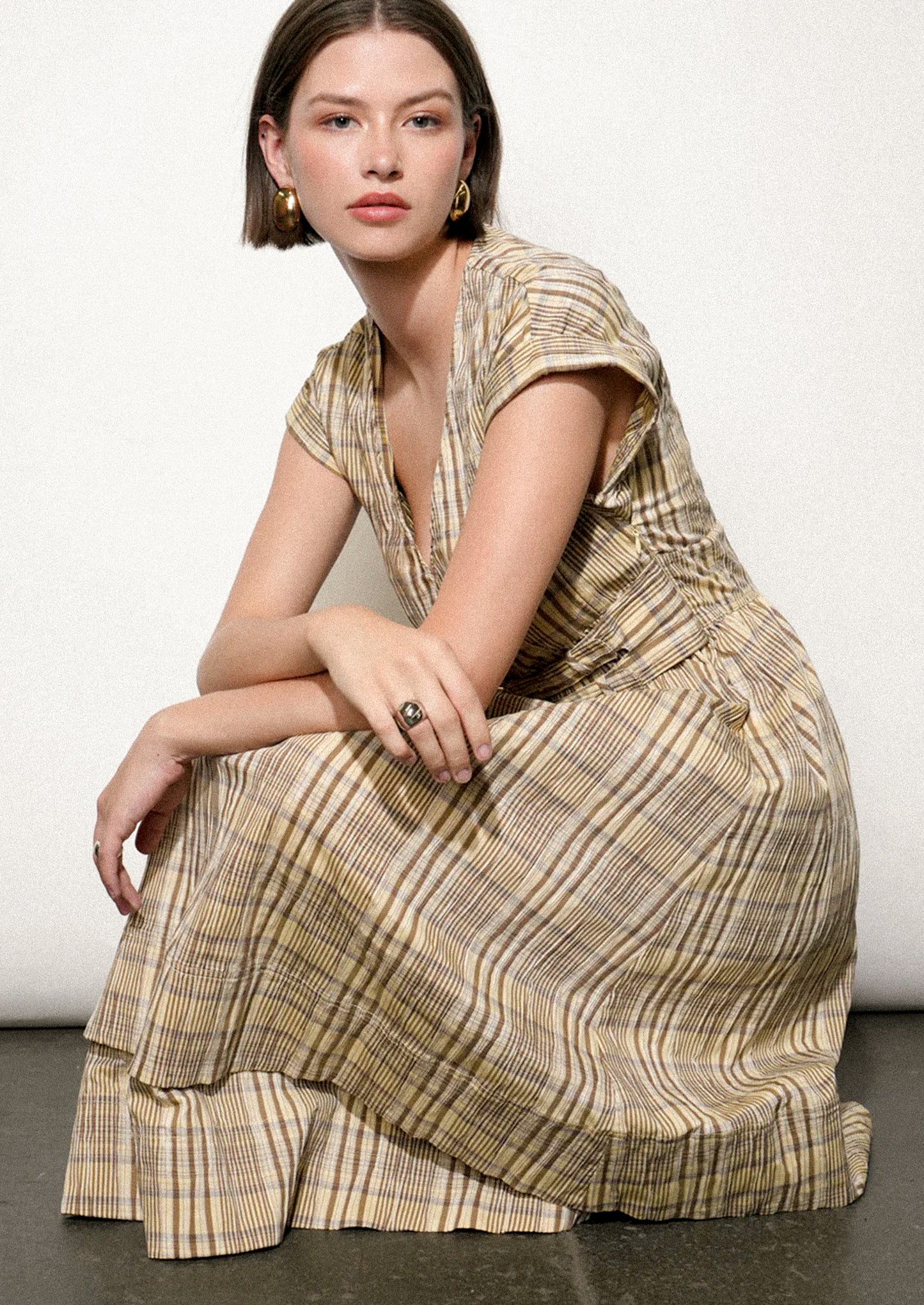 Woman wearing a patterned dress sitting on the floor against a white wall.