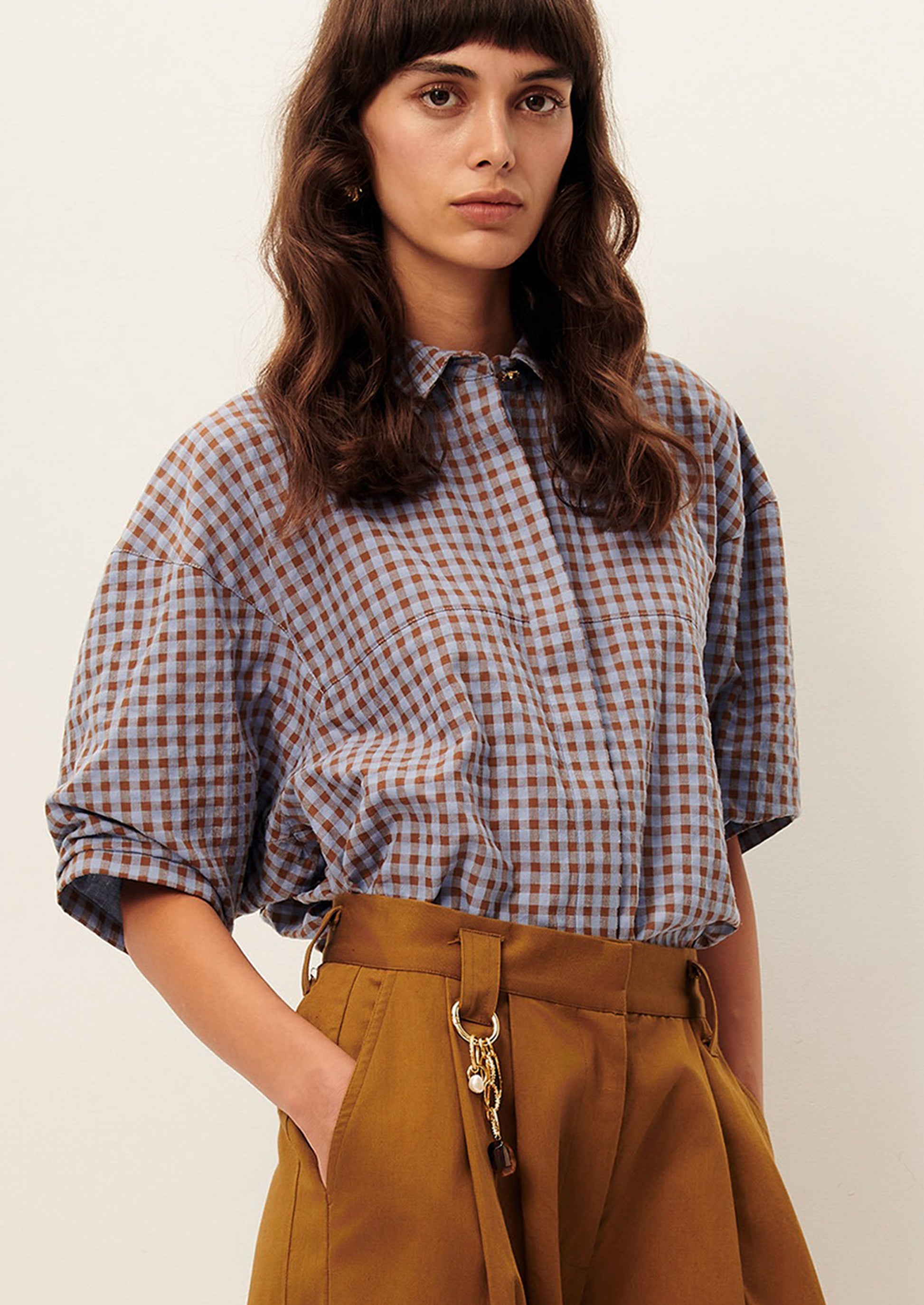 A woman wearing a puff sleeve blouse in brown and periwinkle checker.