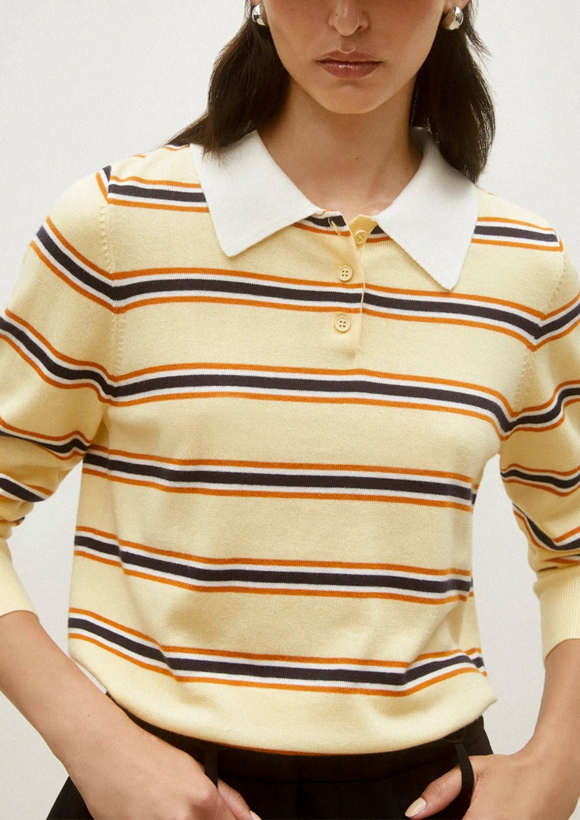 Woman wearing a yellow striped shirt with a white collar against a plain background