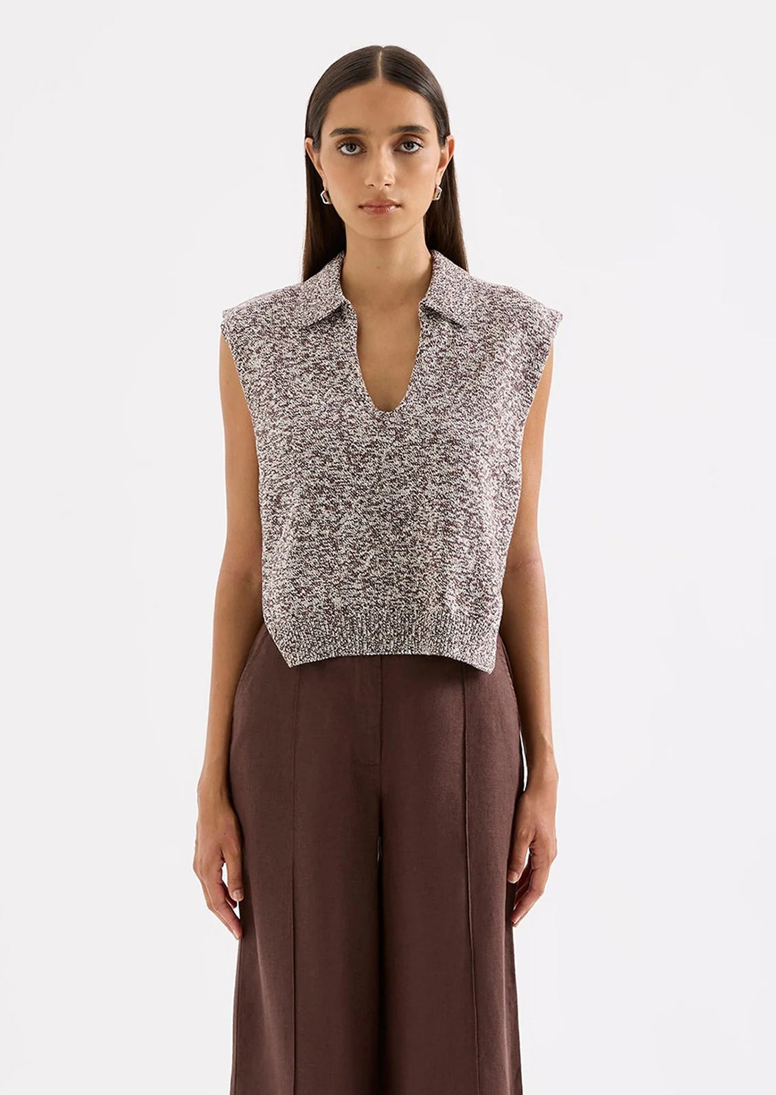 Woman wearing a sleeveless patterned top and brown pants on a white background
