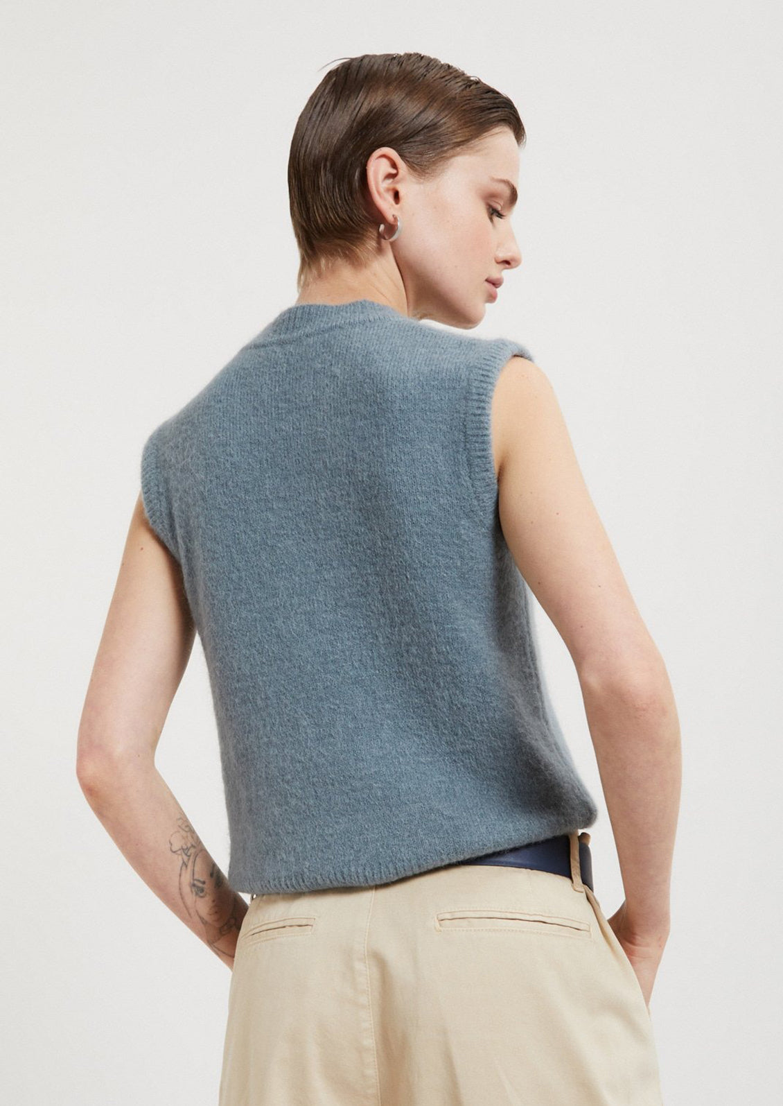 Woman wearing a blue sleeveless sweater against a plain background