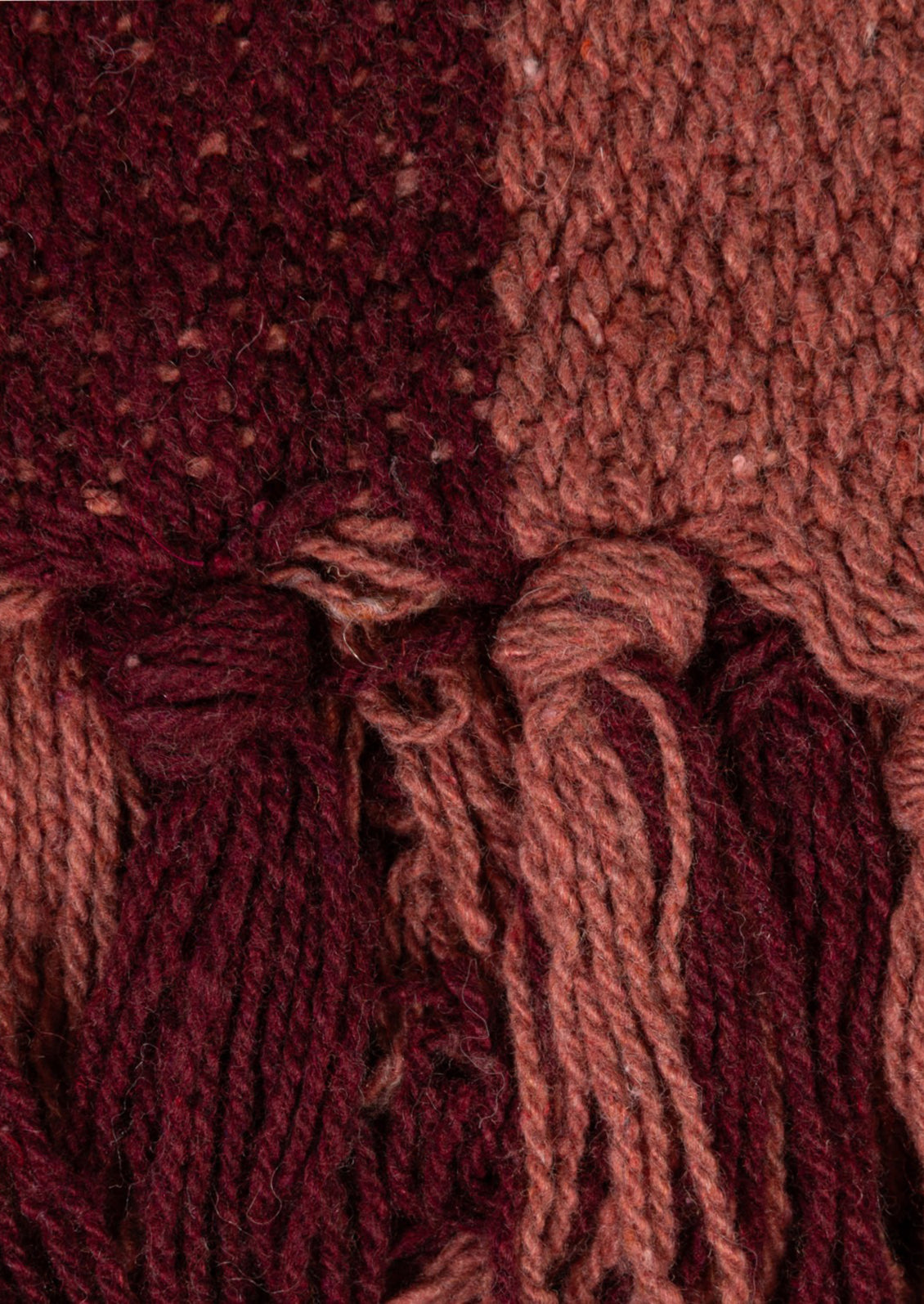 Close-up of a textured knit fabric with tassel fringe in deep burgundy and muted terracotta tones.