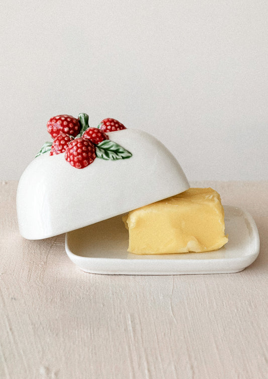 Butter dish with a lid featuring berries on a light wooden surface