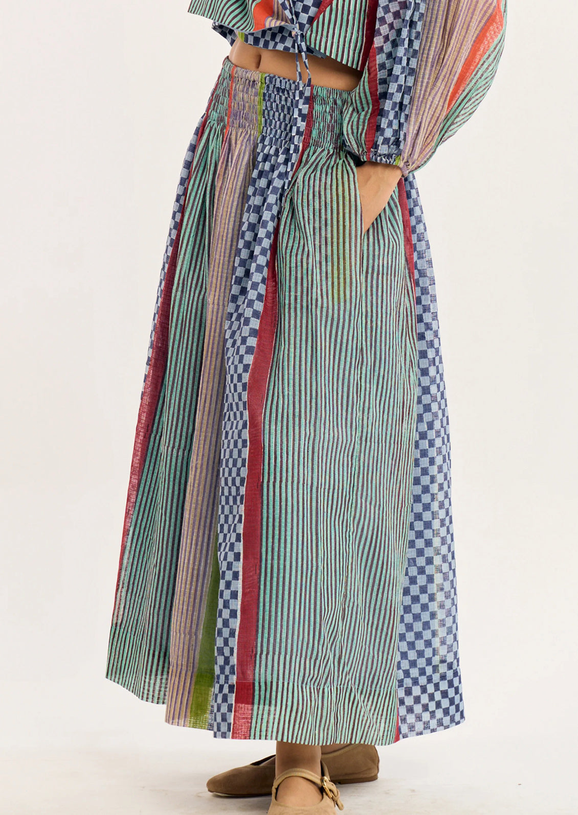 A person wearing a long, multicolored patchwork maxi skirt with vertical stripes, checks, and solid panels in green, blue, red, and beige.