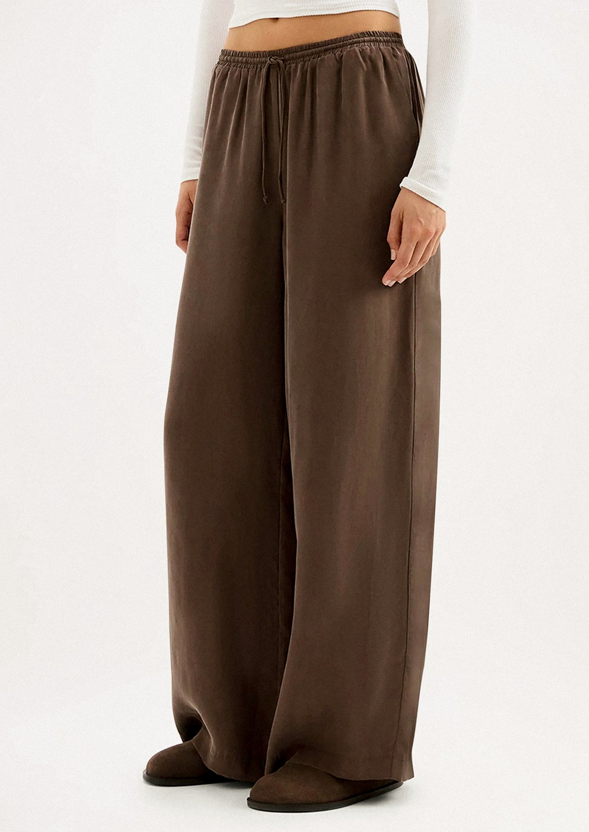 A person wearing a pair of long wide leg pants in brown cupro.