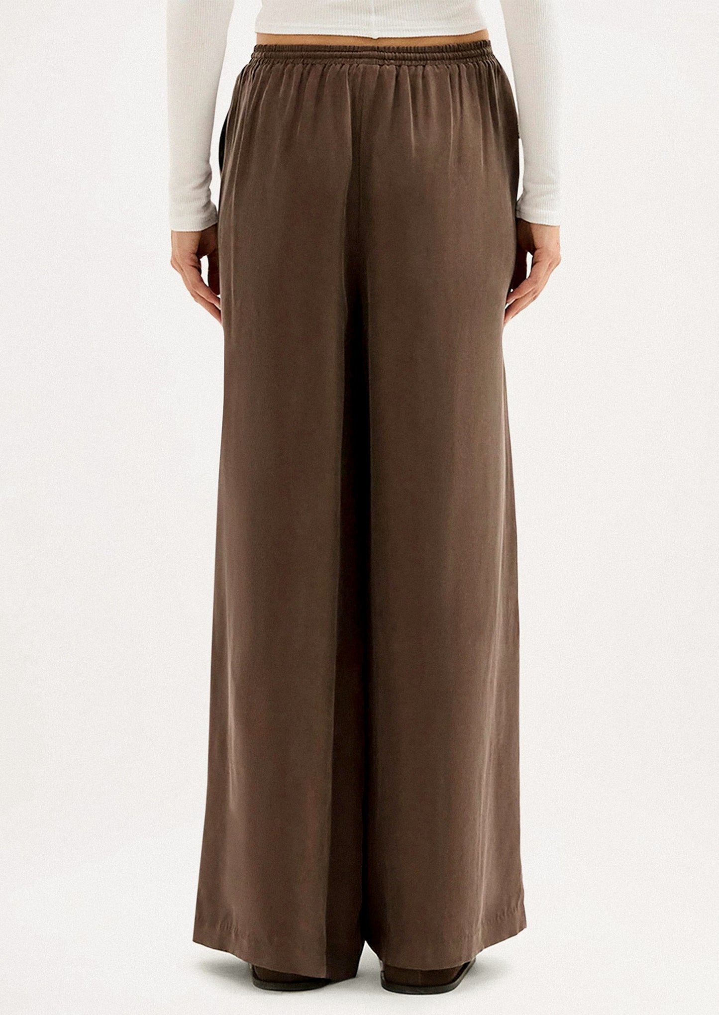 A person wearing a pair of long wide leg pants in brown cupro.