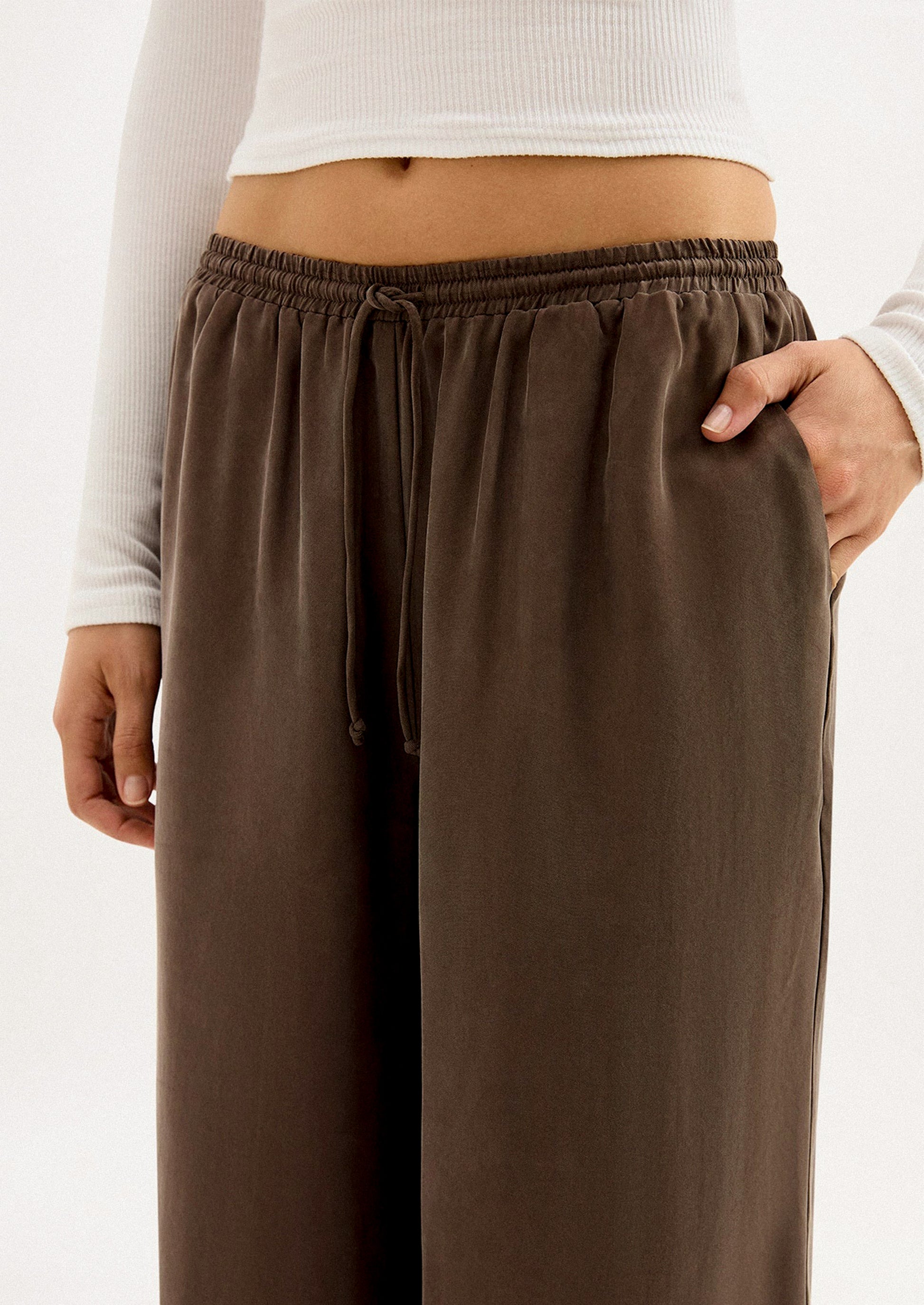 A person wearing a pair of long wide leg pants in brown cupro.