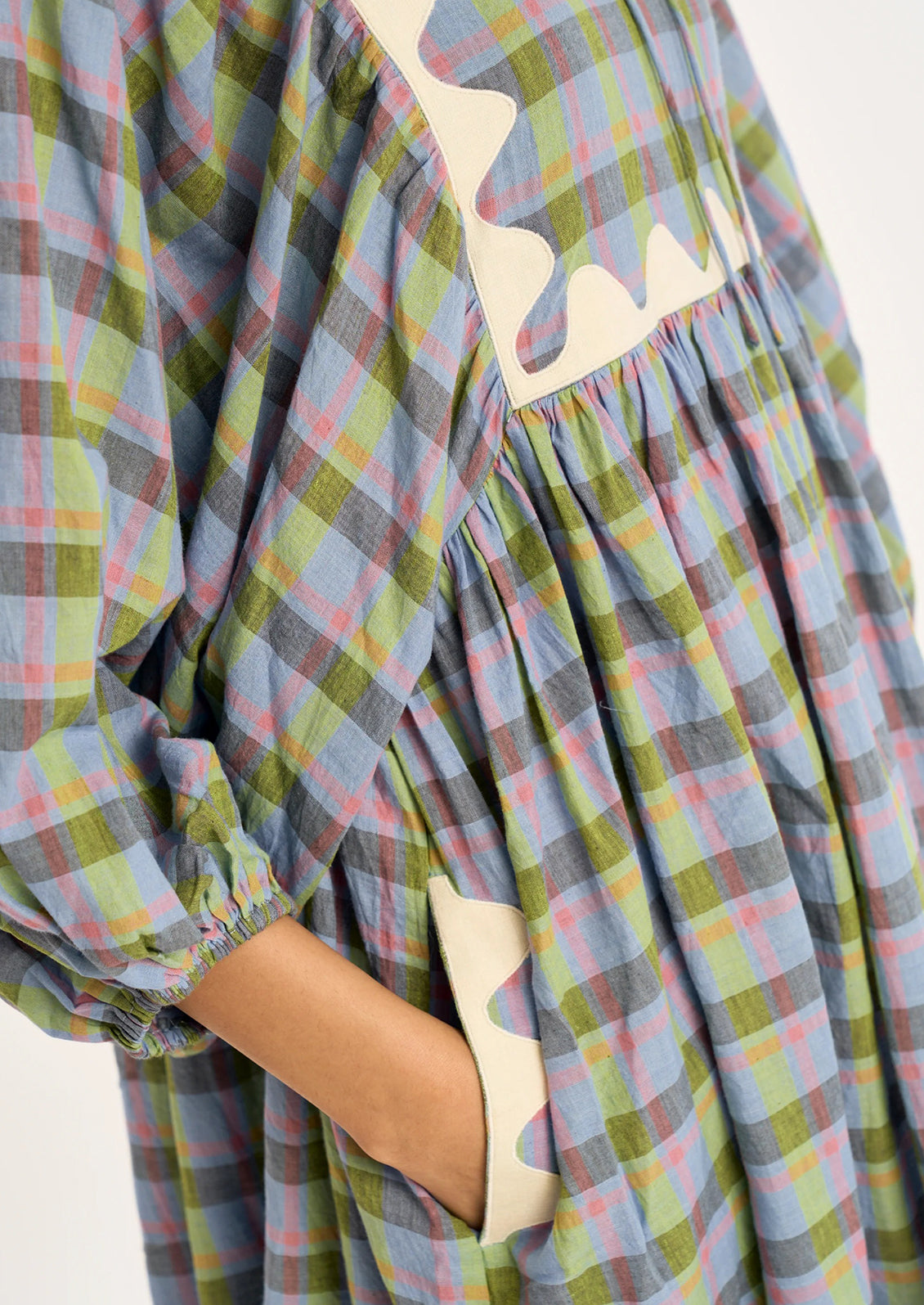 Close-up of a plaid dress with a multicolor pattern of green, blue, pink, and yellow, featuring a cream-colored asymmetrical zipper detail and a side pocket.