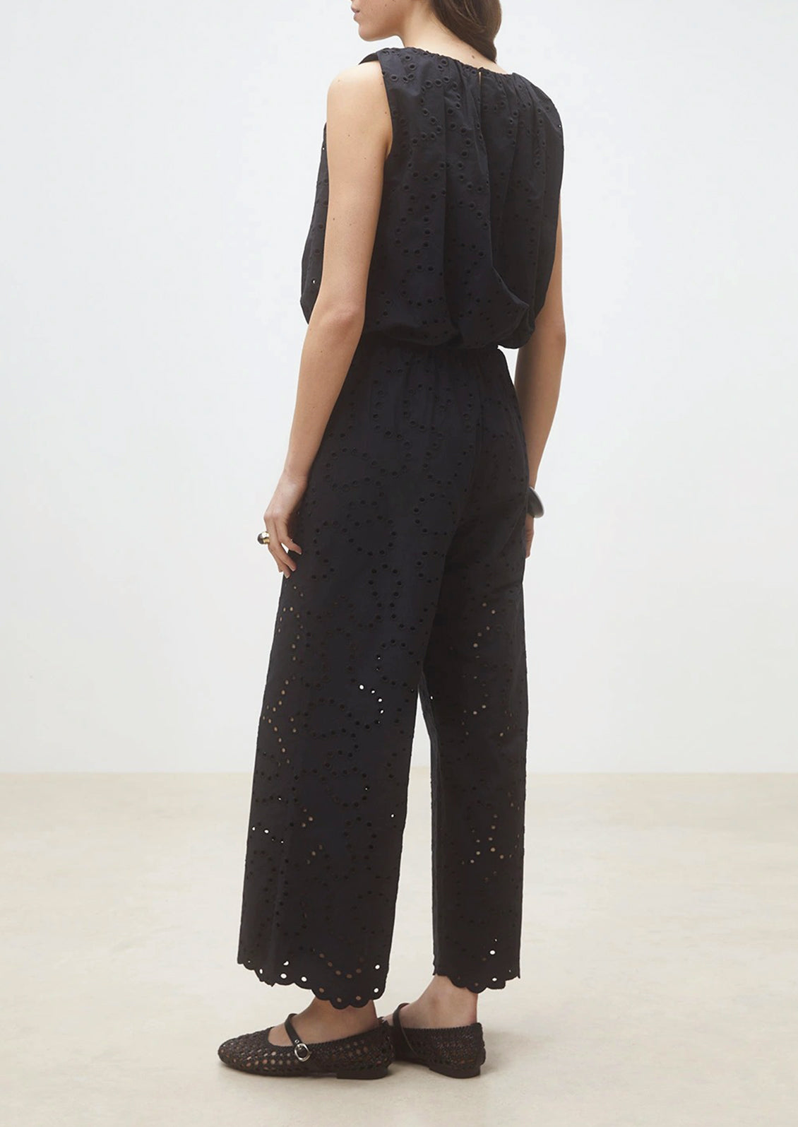 Person wearing a black outfit with intricate detailing on a plain background