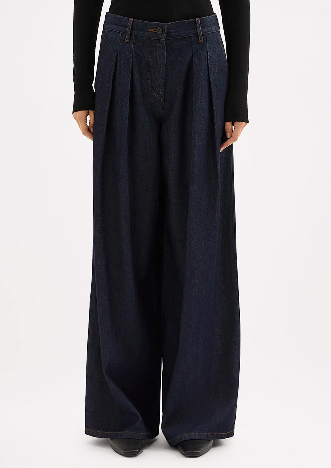 A person wearing a pair of dark rinse wide leg denim trousers with pleated shape.