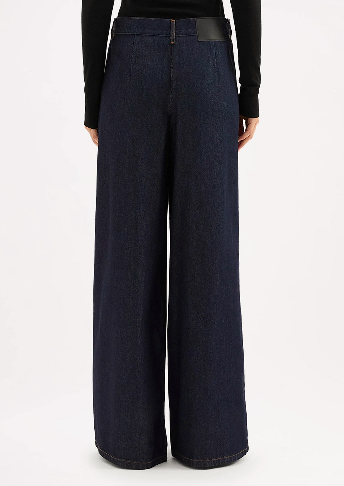 A person wearing a pair of dark rinse wide leg denim trousers with pleated shape.