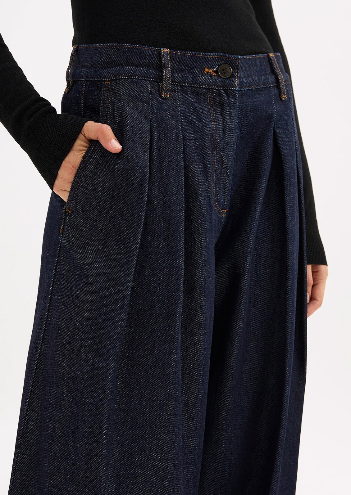 A person wearing a pair of dark rinse wide leg denim trousers with pleated shape.