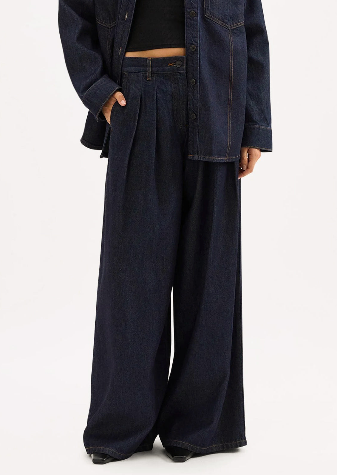 A person wearing a pair of dark rinse wide leg denim trousers with pleated shape.