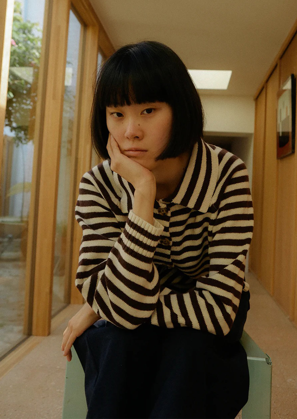 Person wearing a brown and white striped sweater in a room with wooden paneling.