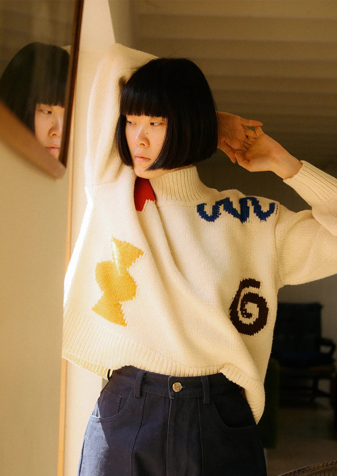 Person wearing a white sweater with colorful designs, standing in front of a mirror.