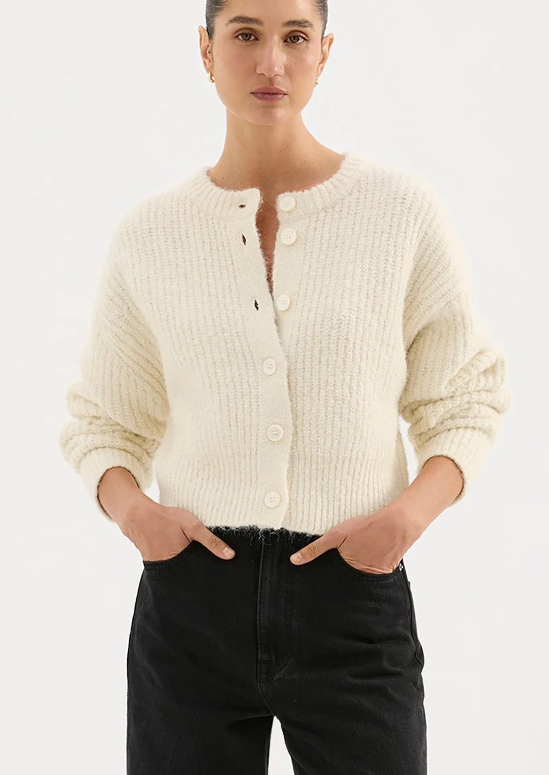 Person wearing a cream cardigan and black pants on a white background