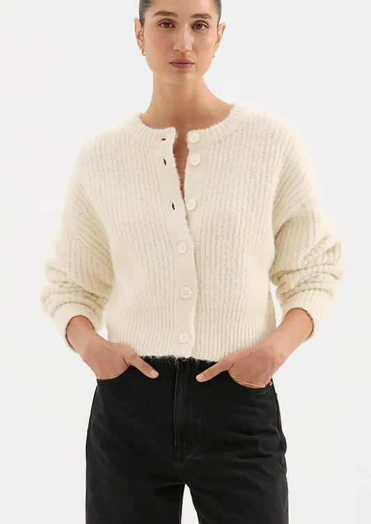 Person wearing a cream cardigan and black pants on a white background