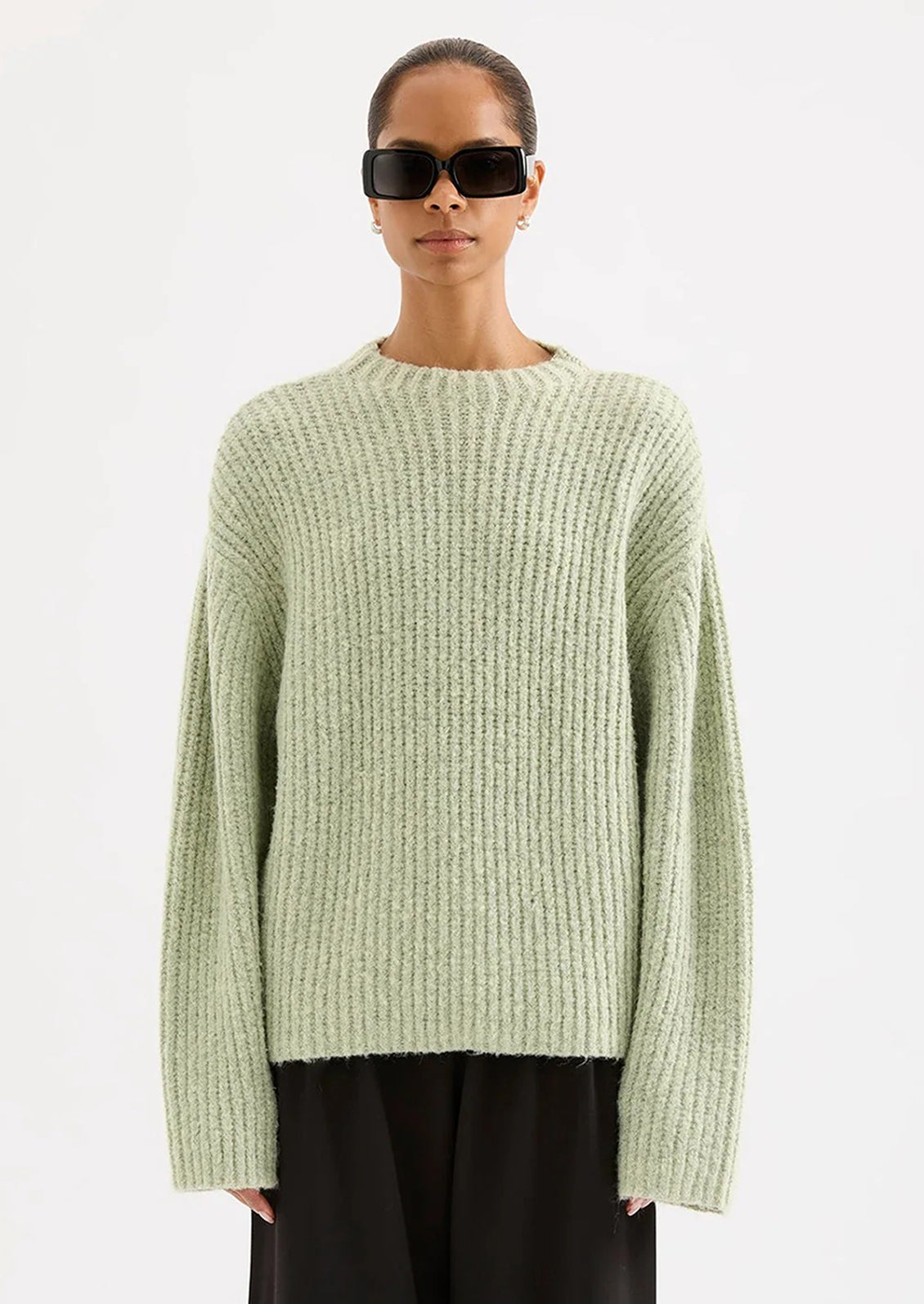 Person wearing a light green sweater and black pants on a white background