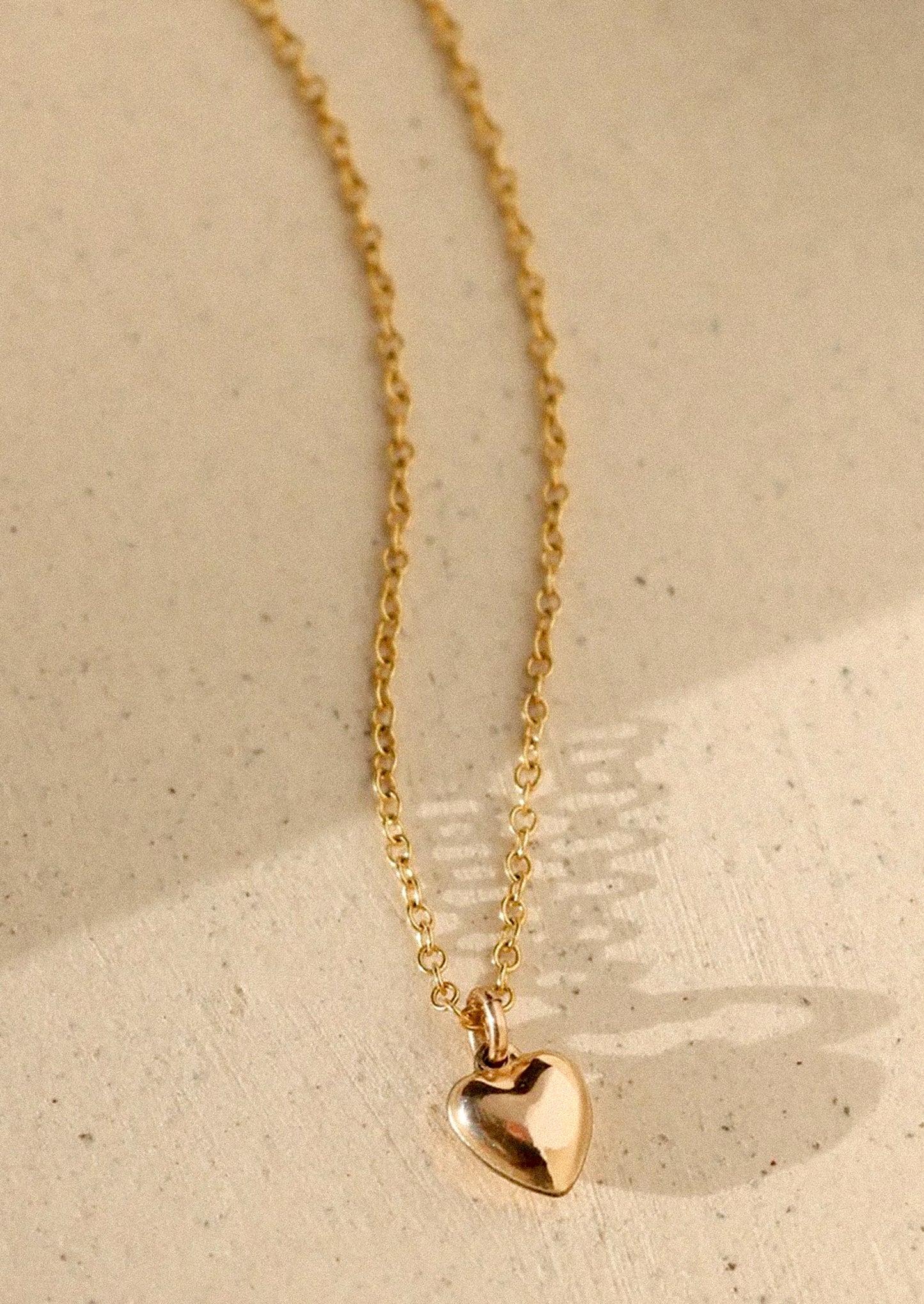 Gold heart-shaped pendant necklace on a beige background