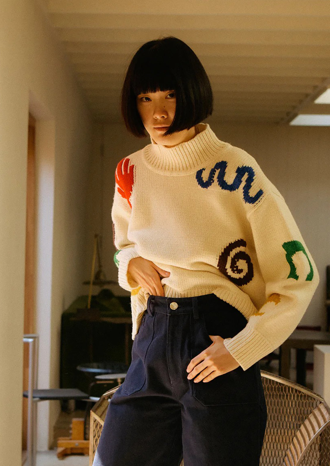Person wearing a cream sweater with colorful patterns in an indoor setting