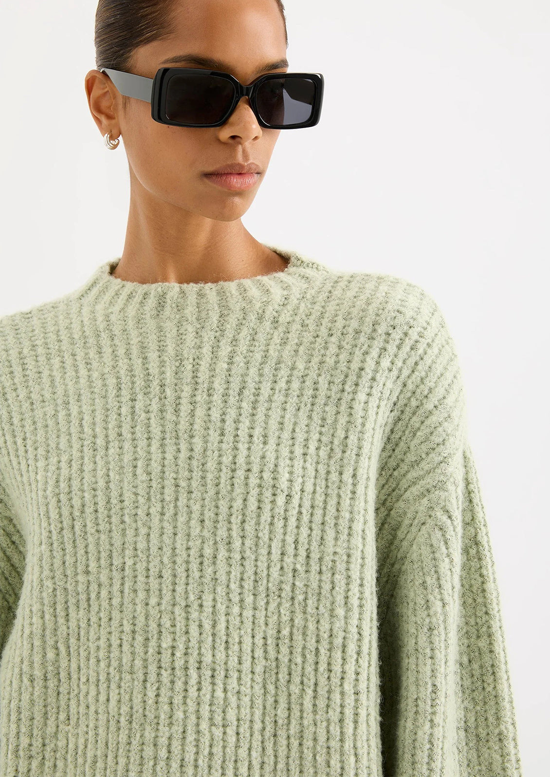 Person wearing a light green sweater and black sunglasses on a white background