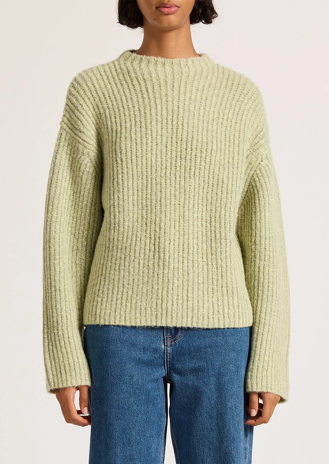 Person wearing a light green sweater and blue jeans on a plain background