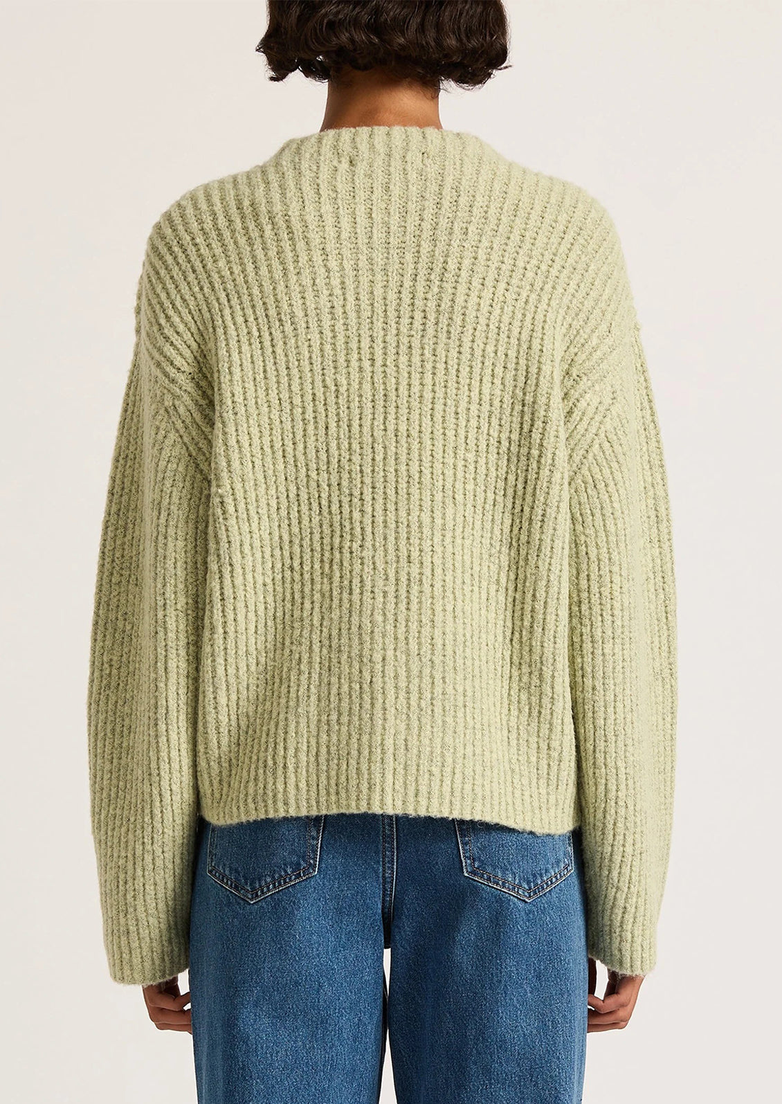 Person wearing a light green sweater and blue jeans on a plain background