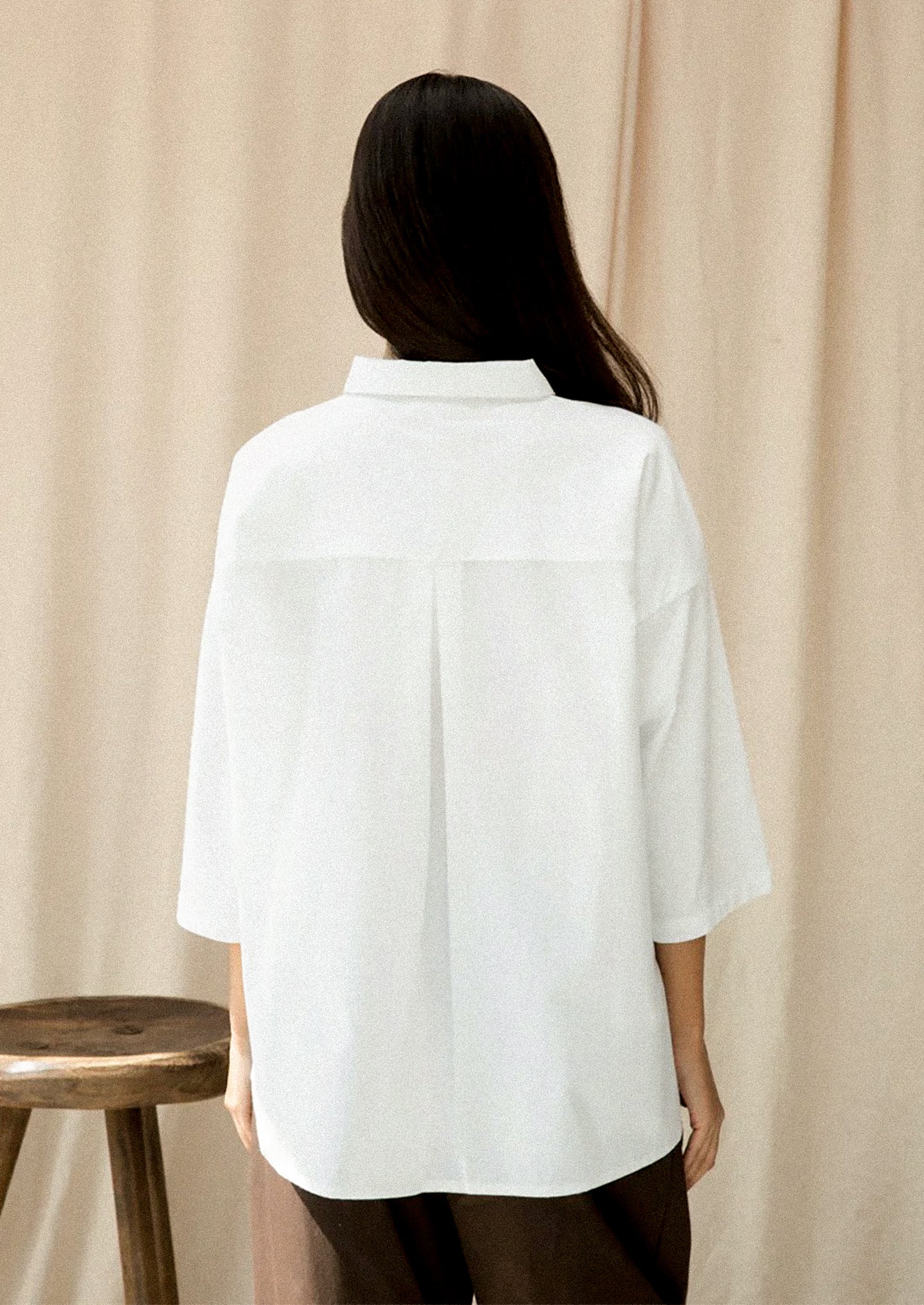 Person wearing a white shirt standing against a beige curtain