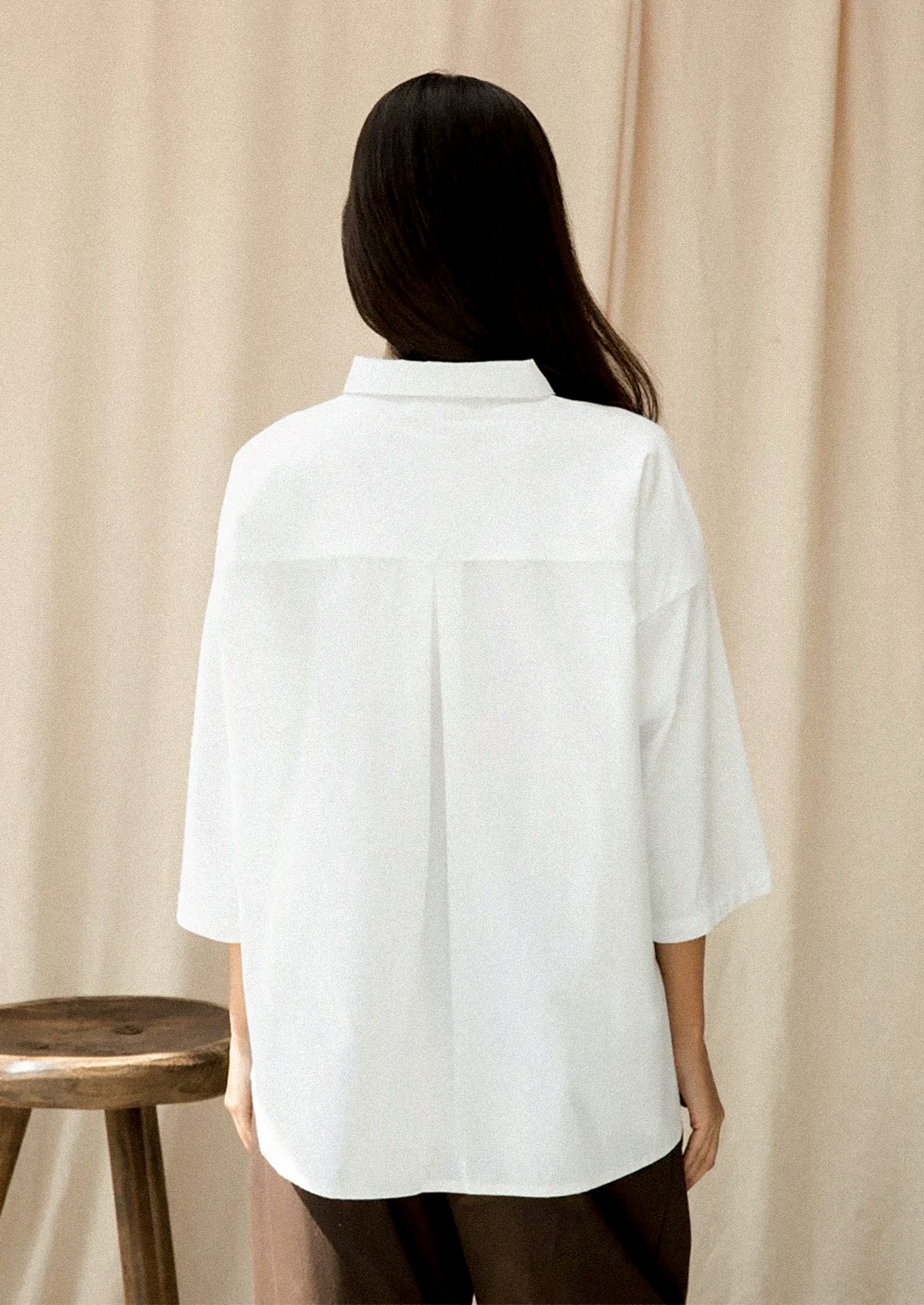 Person wearing a white shirt standing against a beige curtain