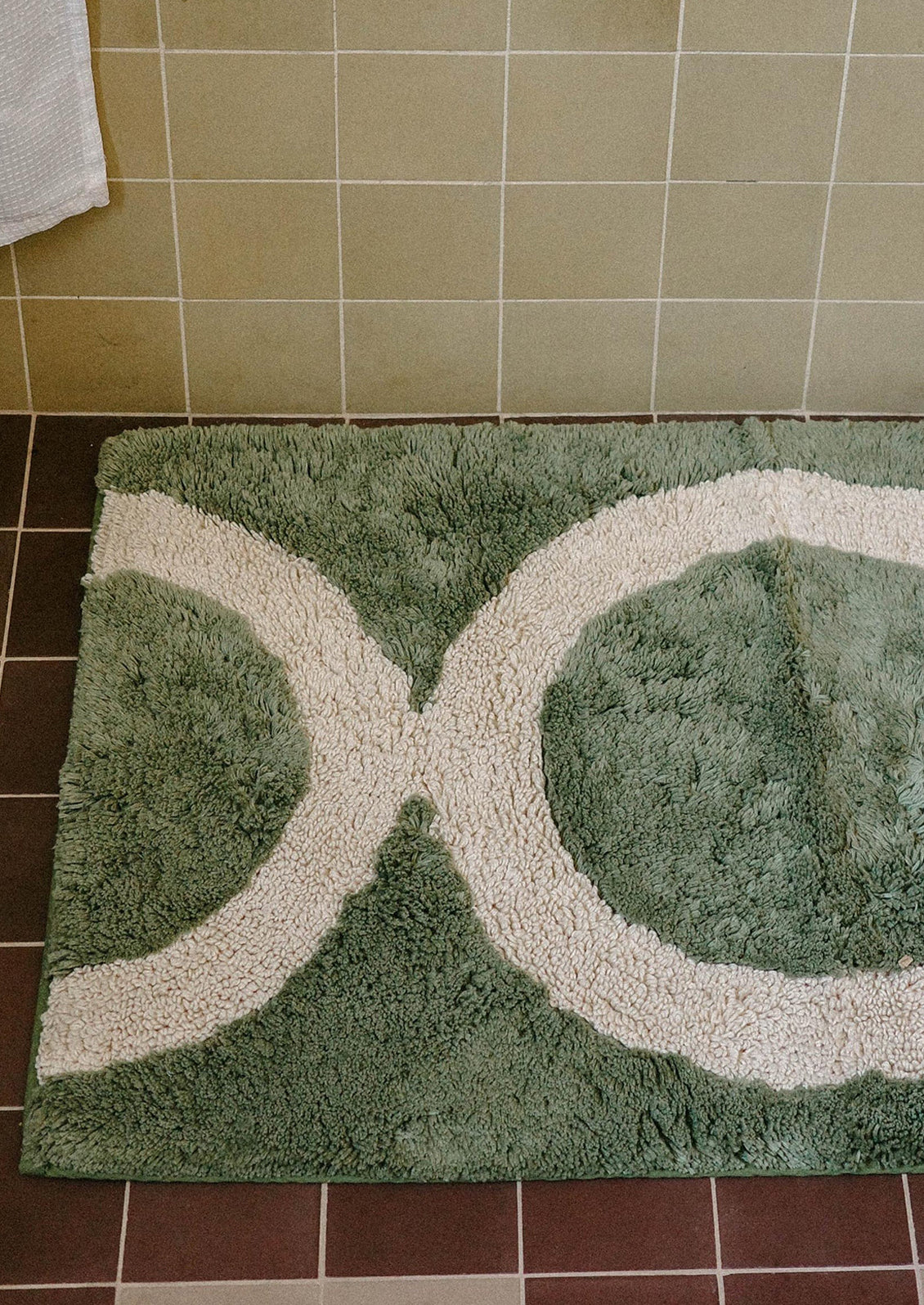 Green and white bath mat with circular design on a tiled bathroom floor.