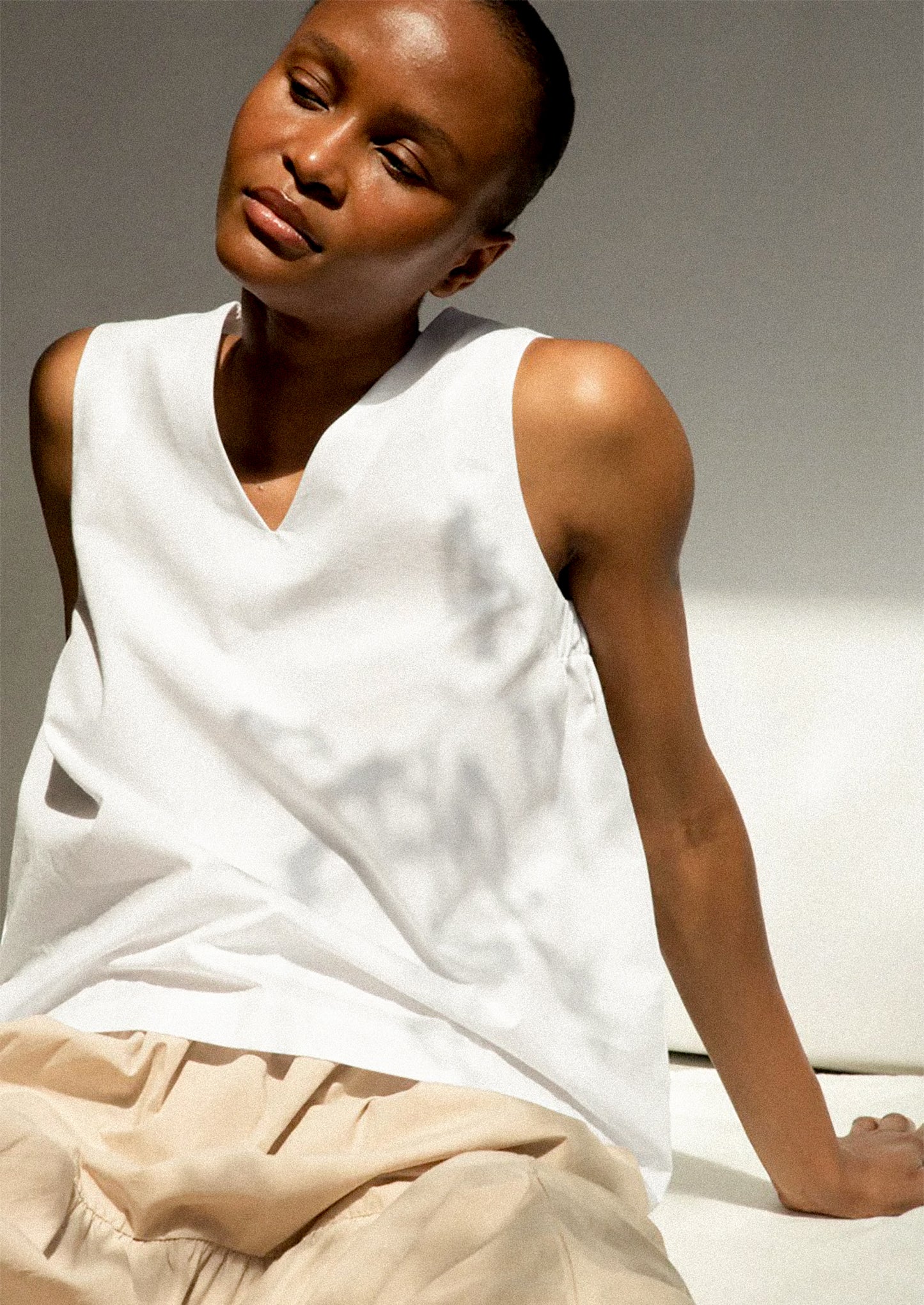 Woman wearing a white sleeveless top and beige pants against a neutral background