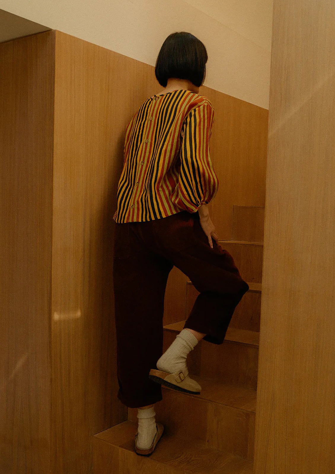 Person in a striped shirt and dark pants ascending a wooden staircase.