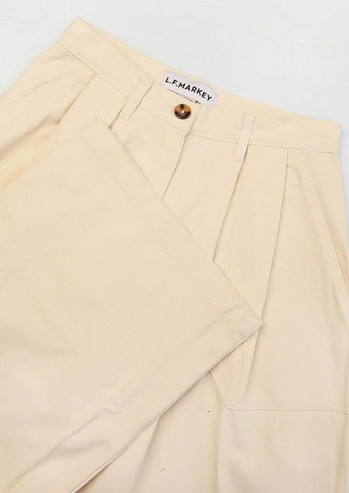 A pair of cream colored trousers with pleat front.