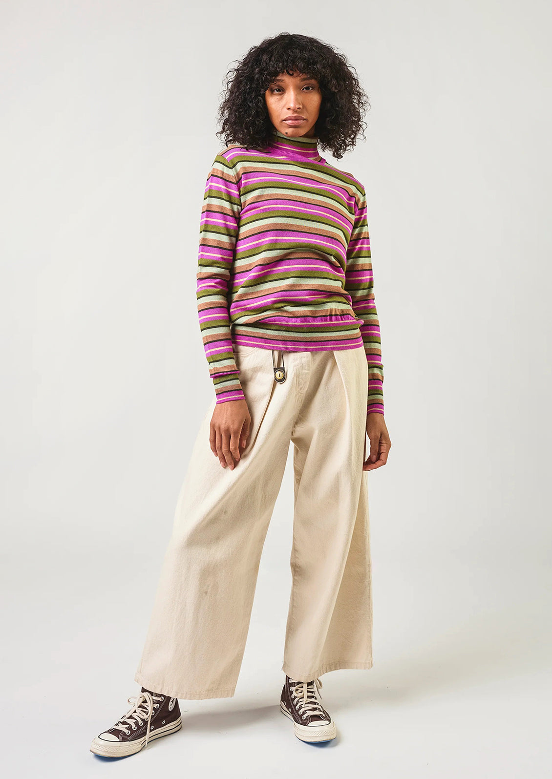 Person wearing a striped sweater and beige pants on a white background