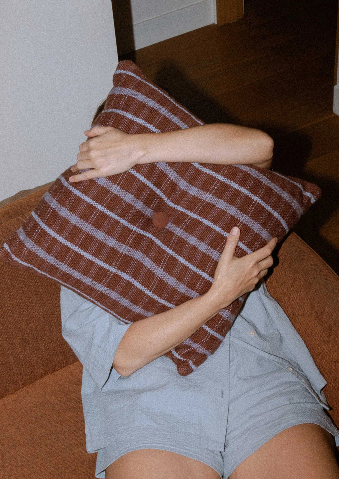 A brown and purple striped cotton pillow with tufted button detail at center.