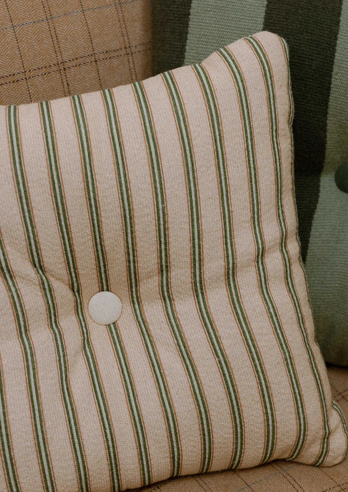 A beige pillow with green stripes and tufted button detailing at center.