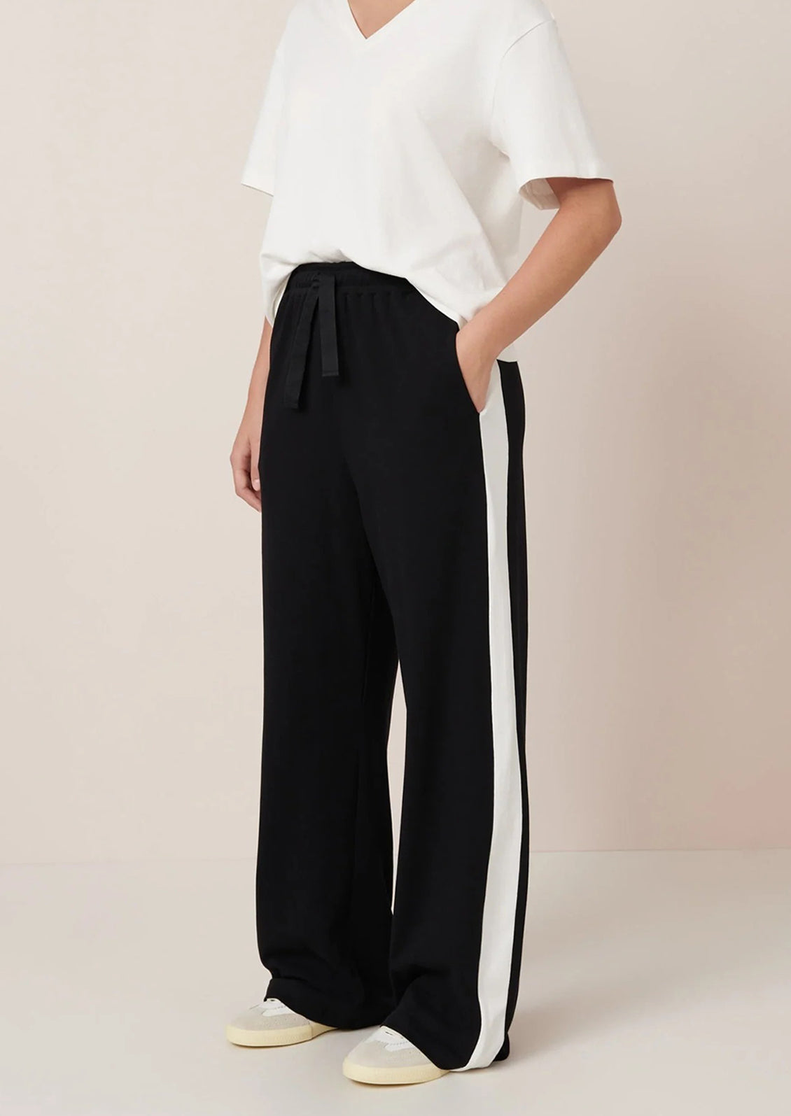 Person wearing black pants with a white stripe on a beige background