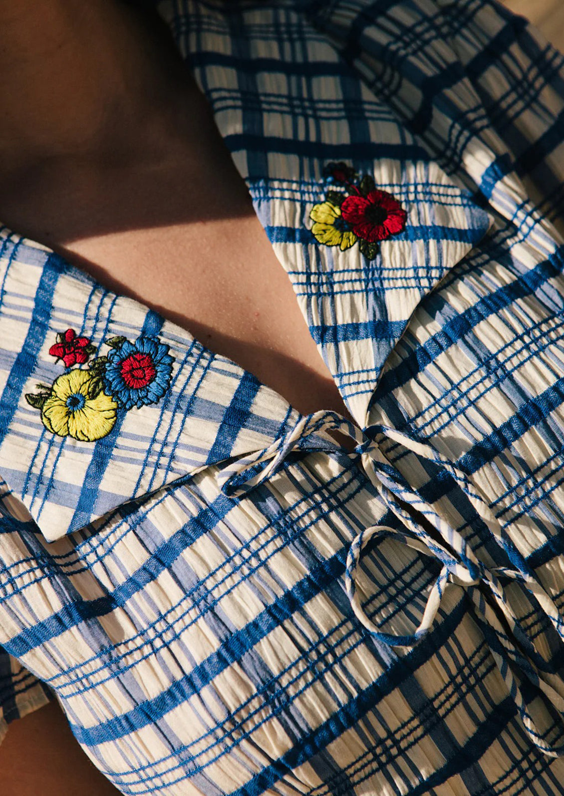 A blue and white plaid mini dress with primary colored floral embroidery at collar.