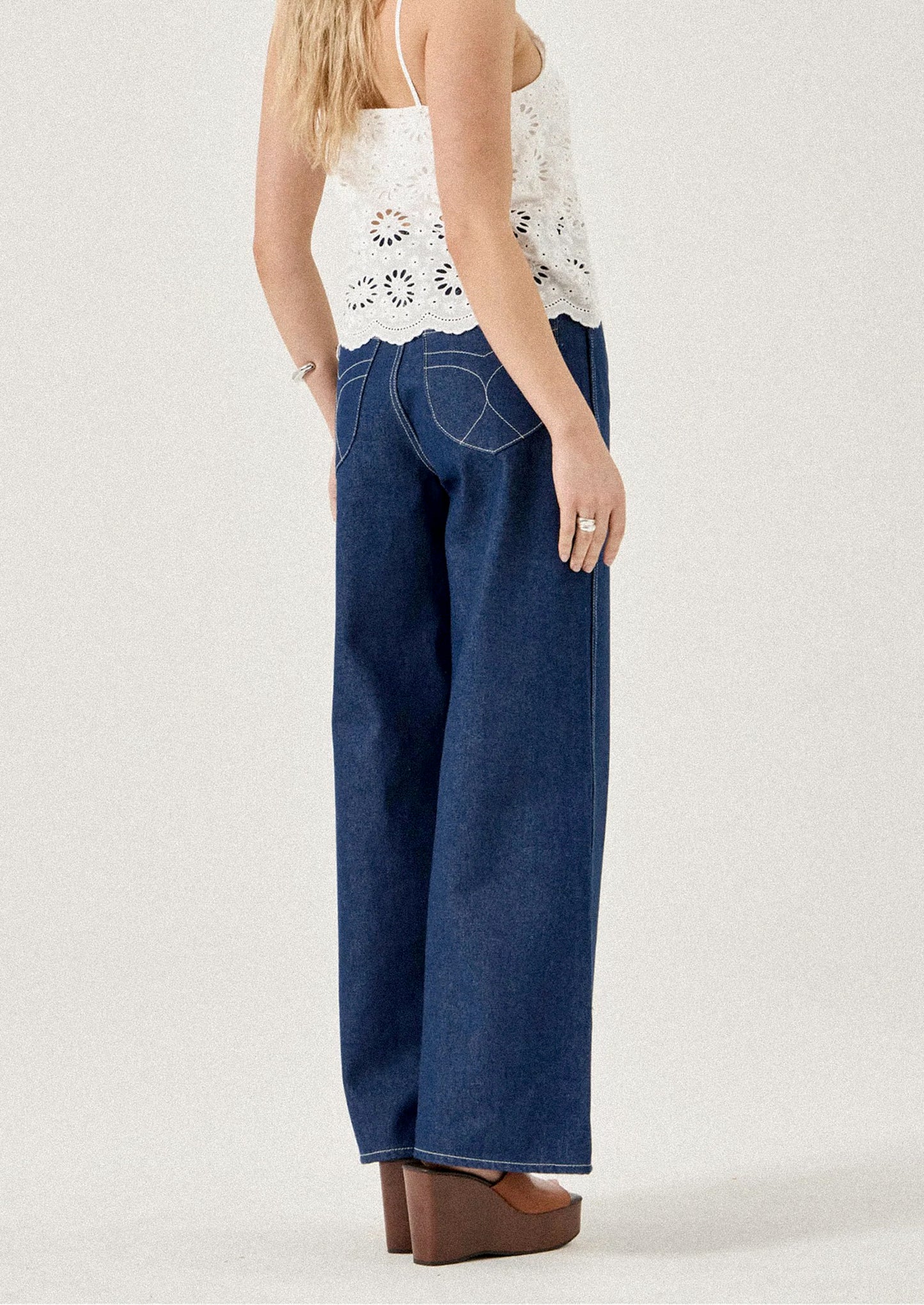 Woman wearing blue denim pants and a white lace top on a plain background