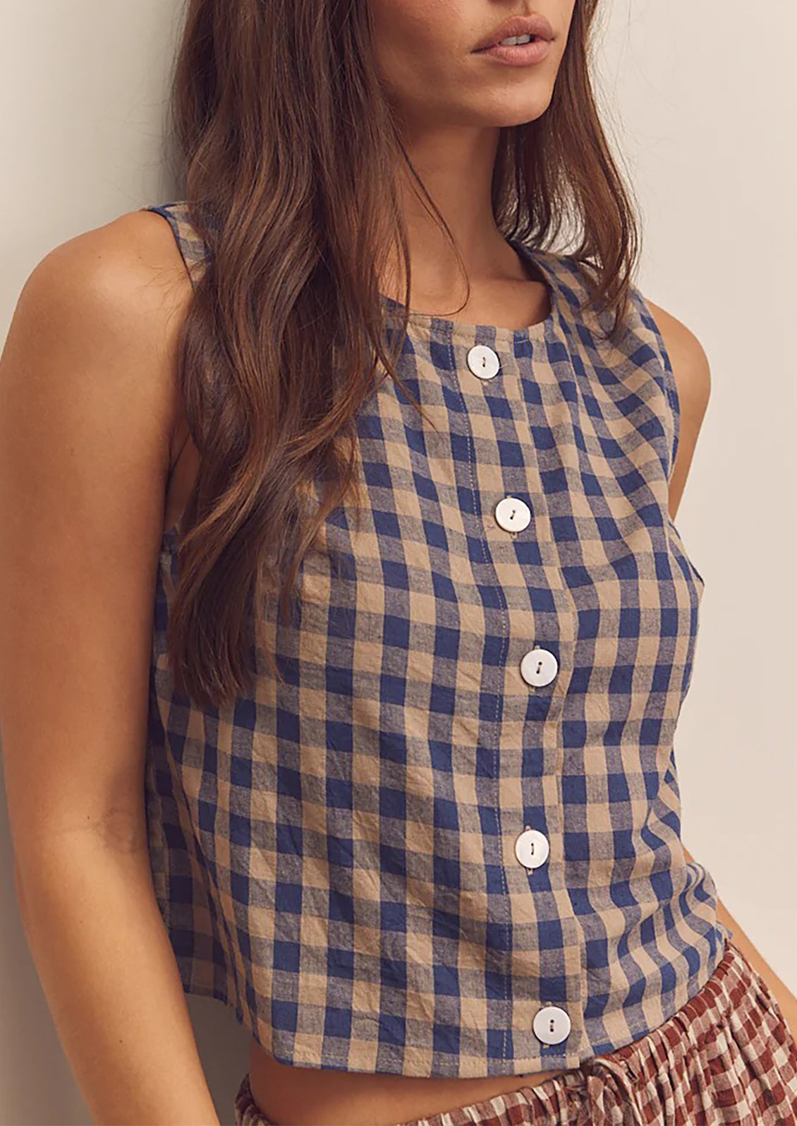 A person wearing a beige and blue gingham top with button front closure.