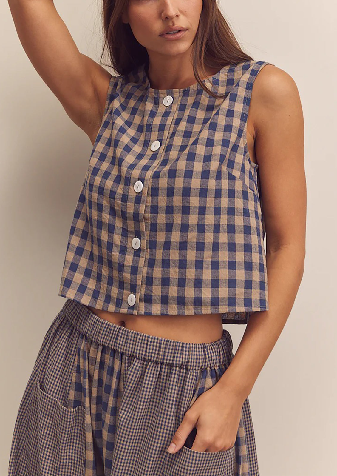 A person wearing a beige and blue gingham top with button front closure.