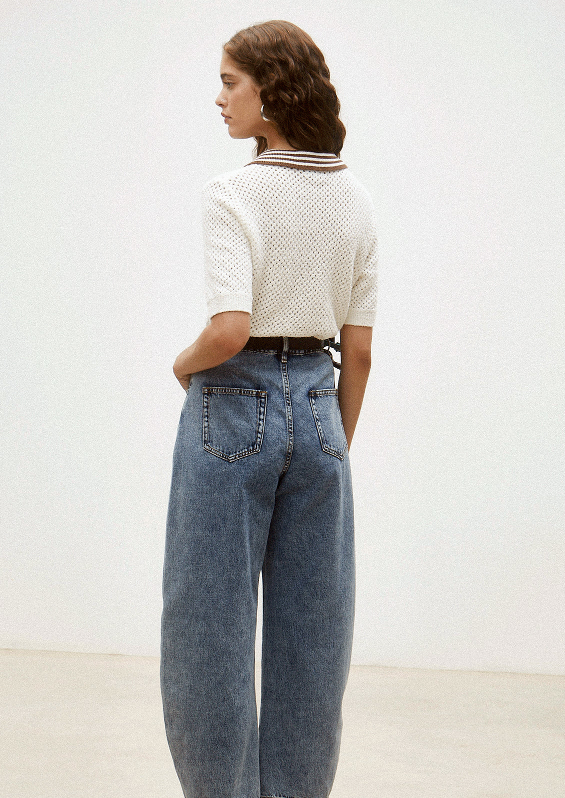 Person wearing a white textured shirt and blue jeans against a plain background