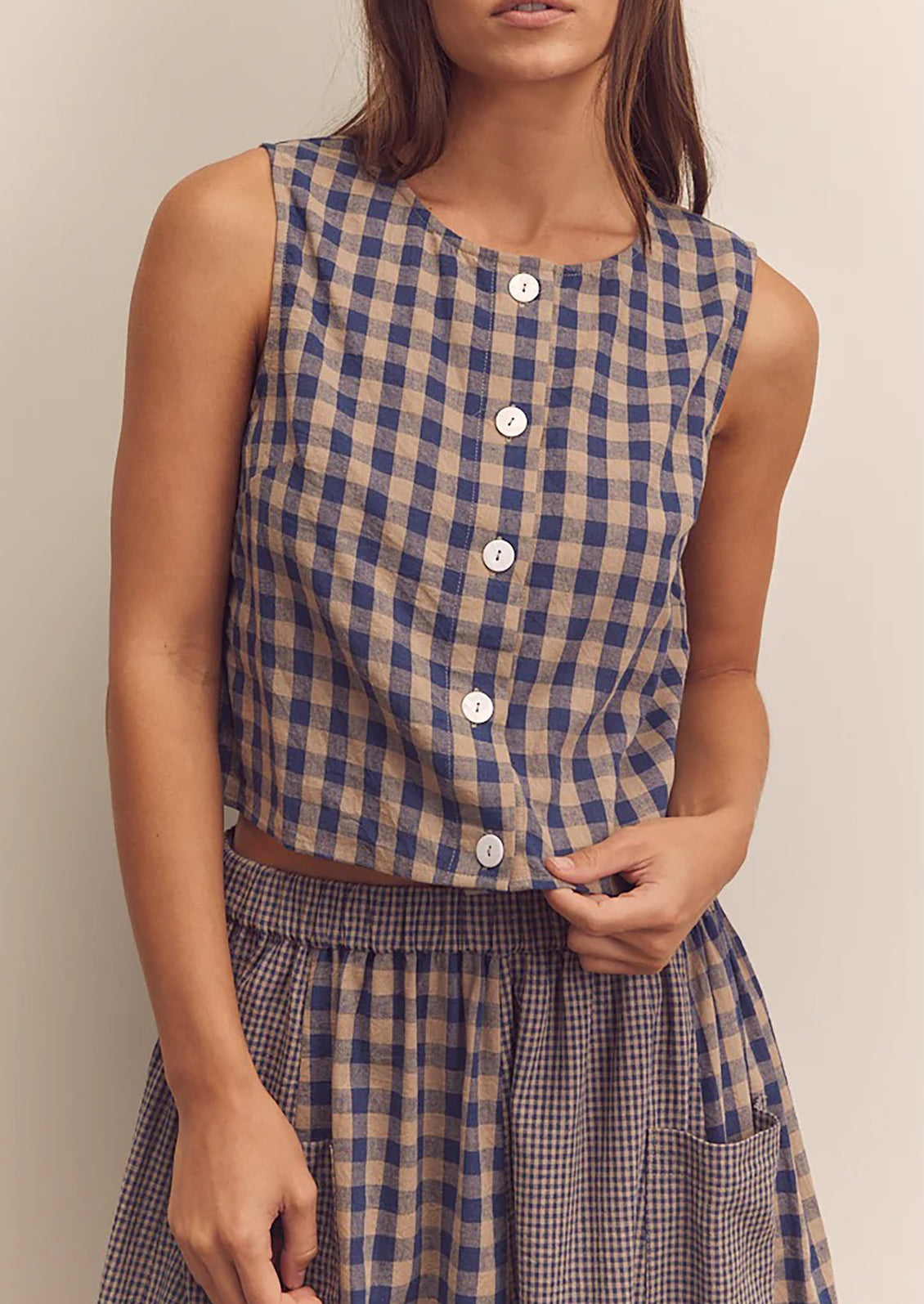 A person wearing a beige and blue gingham top with button front closure.