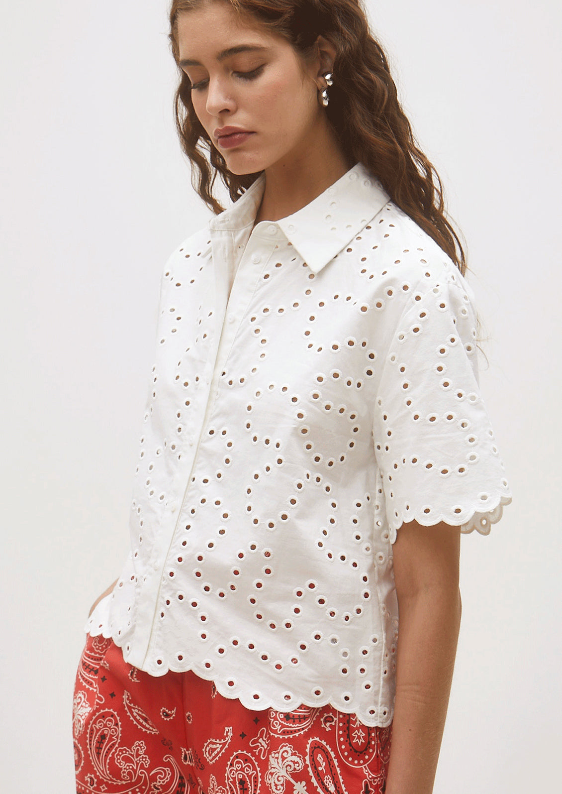 Woman wearing a white blouse with eyelet details and red patterned pants on a white background