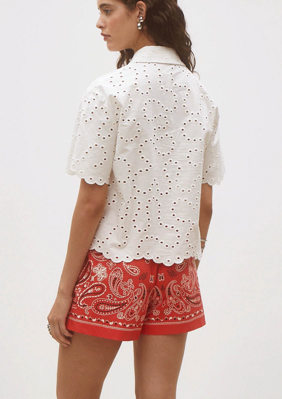 Woman wearing a white embroidered blouse and red paisley shorts on a white background