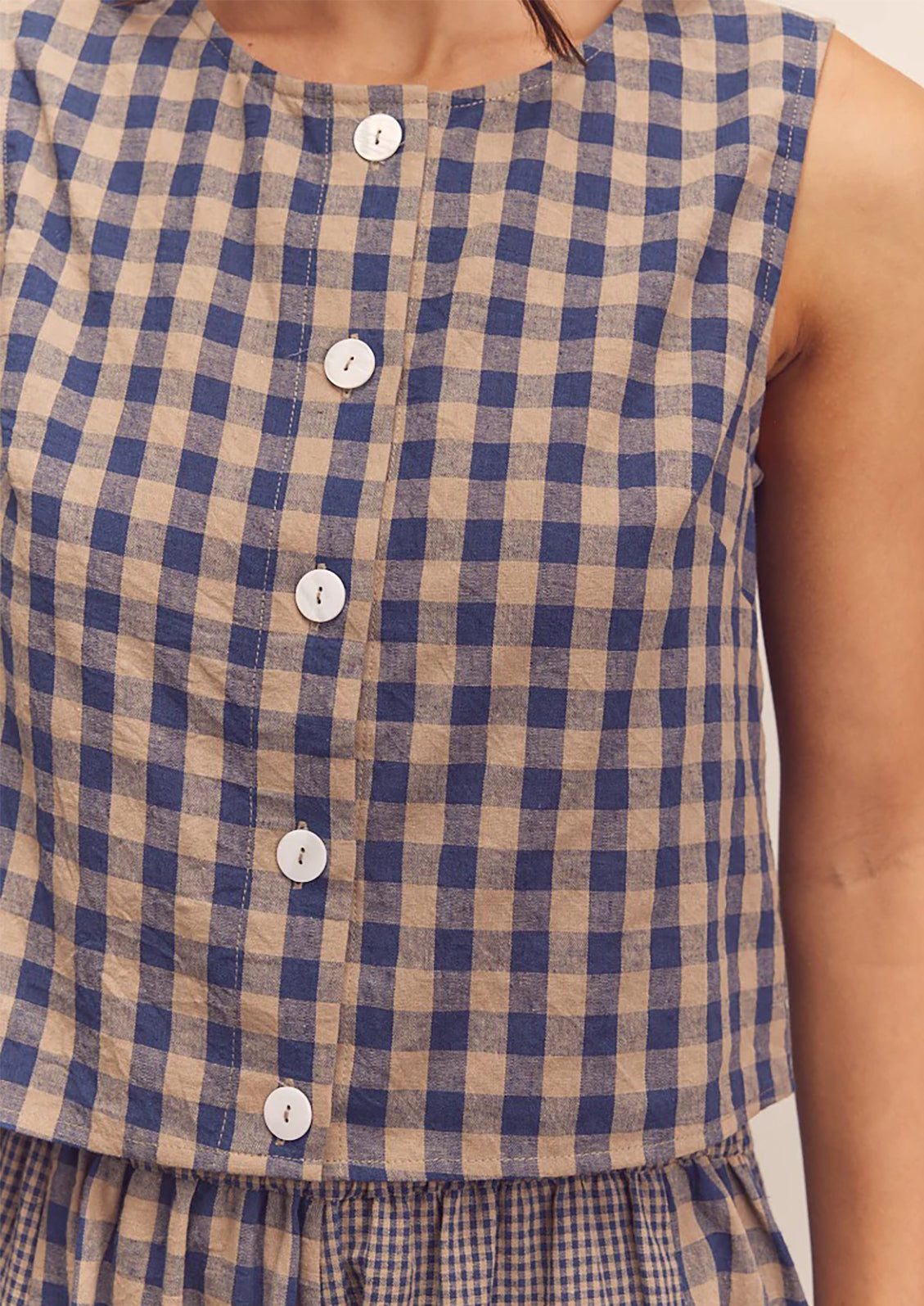A person wearing a beige and blue gingham top with button front closure.