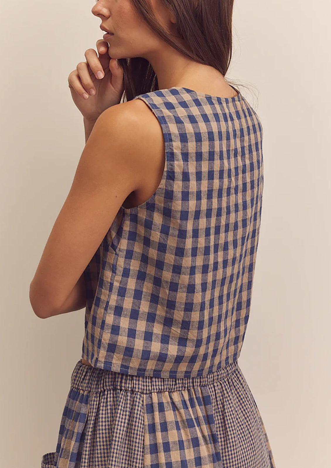 A person wearing a beige and blue gingham top with button front closure.