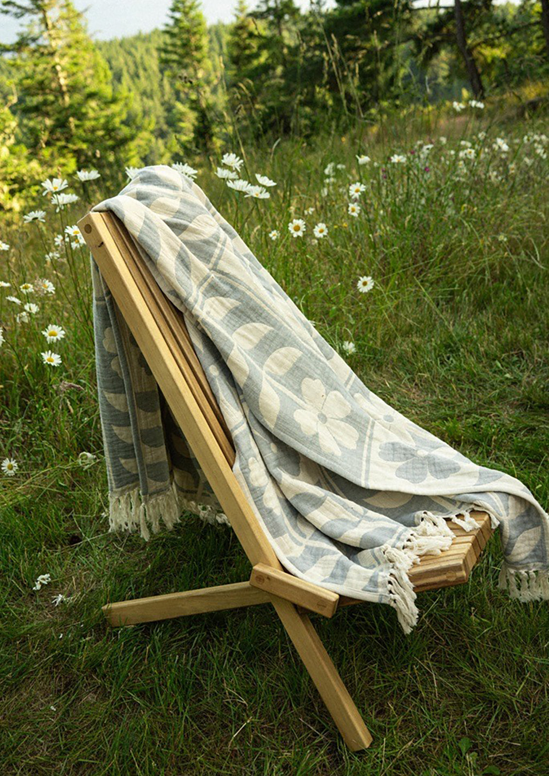 Wooden chair with a patterned blanket in a grassy field with wildflowers