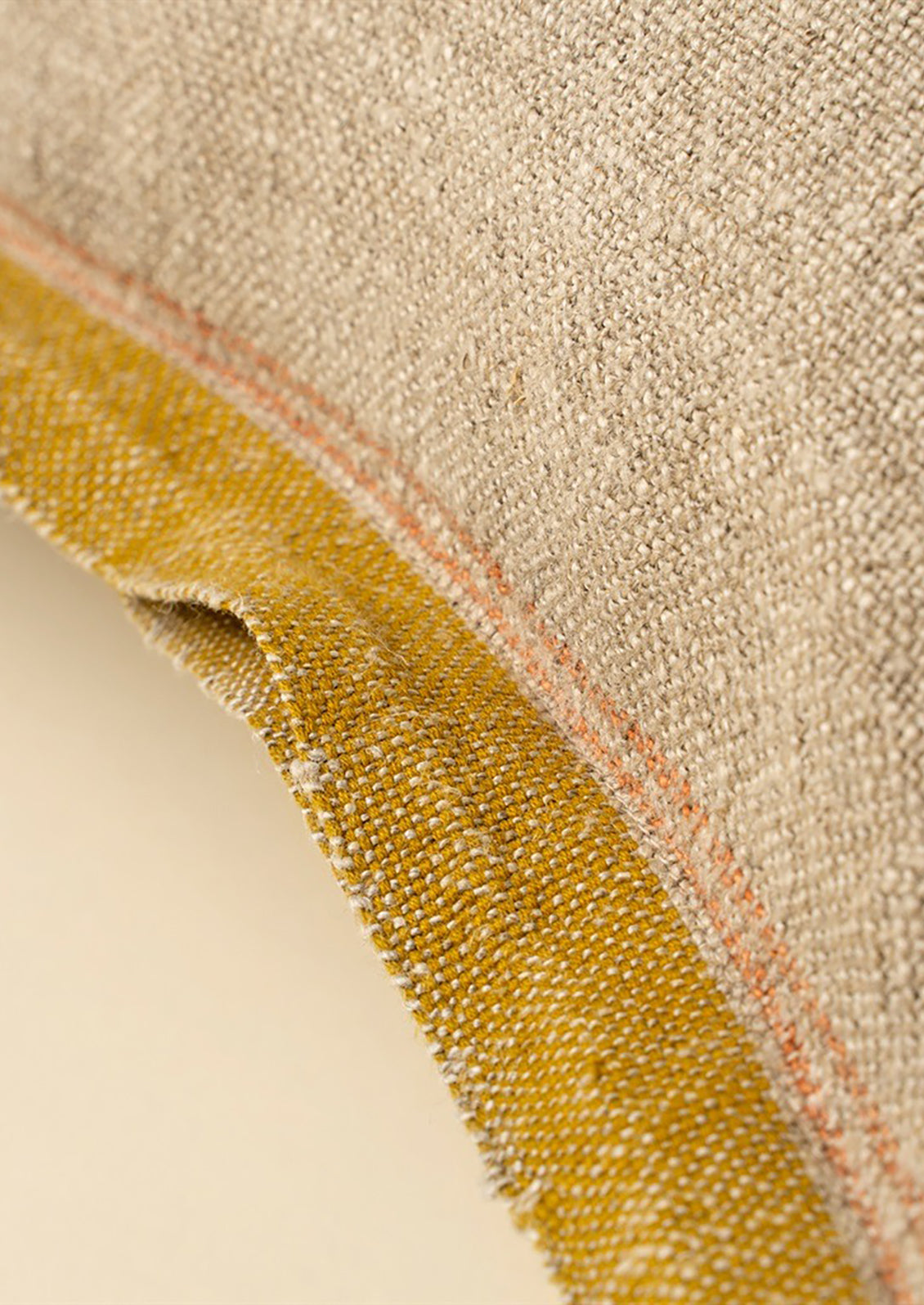 A natural linen throw pillow with mustard decorative selvage trim.
