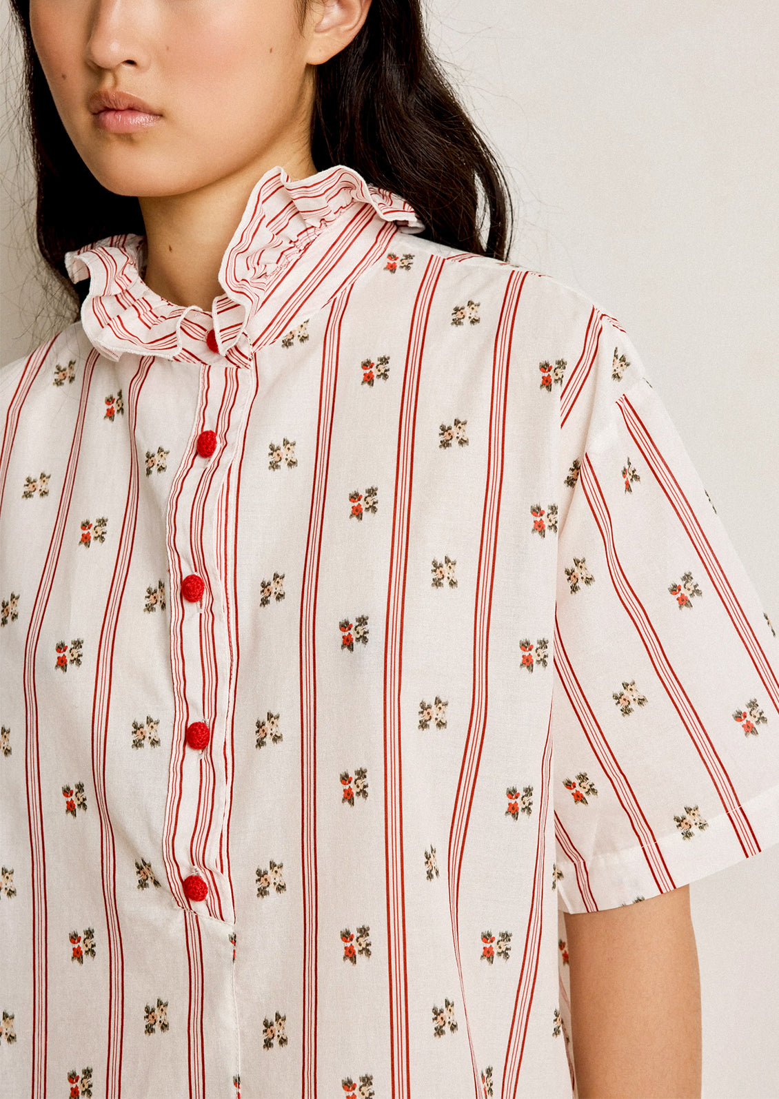 Woman wearing a white blouse with red stripes and floral patterns on a plain background
